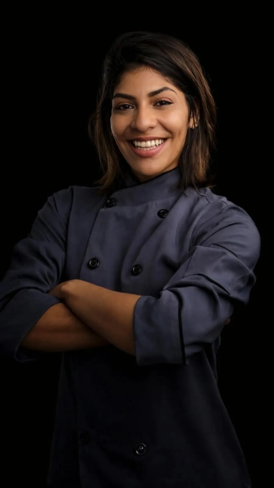 Retrato da Joy, de braços cruzados, com a jaqueta de chef